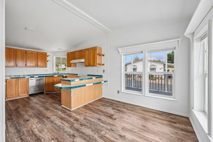 Kitchen featuring wood-finish flooring, wood cabinetry, stainless steel dishwasher, and a built-in breakfast bar with tiled countertop