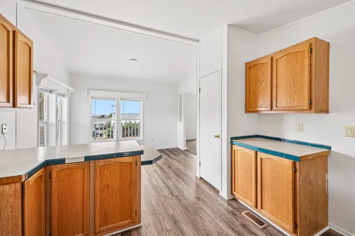 Wood-finish flooring throughout, white walls, and wood cabinetry with tiled countertops
