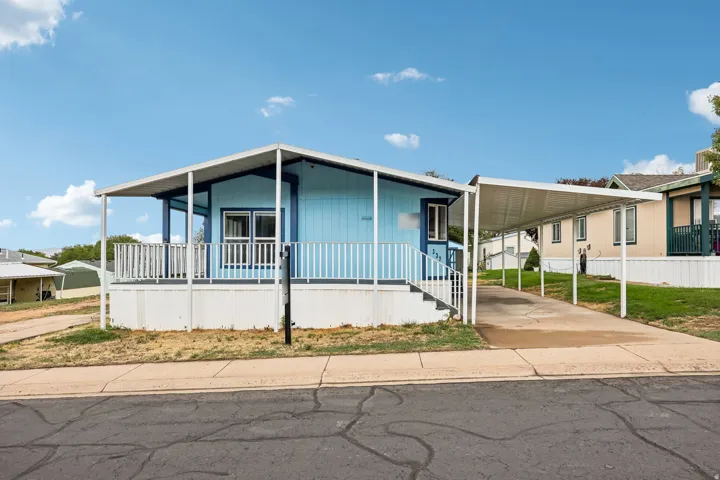 Light blue exterior with white trim, covered front porch, carport, and paved driveway