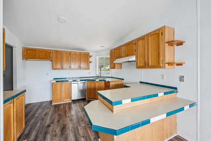 Kitchen featuring wood-finish cabinetry, tile countertops, stainless steel dishwasher, and wood-finish flooring