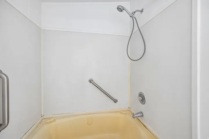 Tub and shower combination with a flexible showerhead, wall-mounted fixtures, and two grab bars