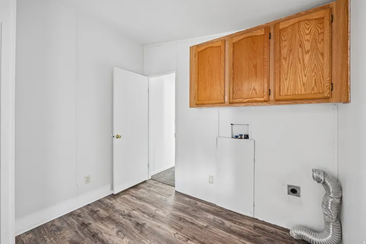 Wood-finish flooring, overhead cabinetry, and panel walls with a door leading into an additional room