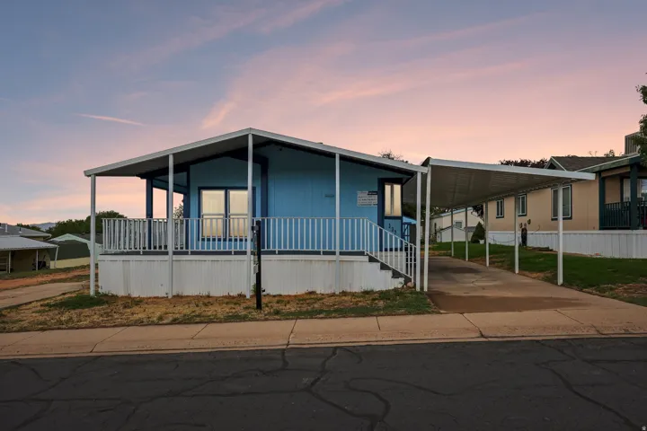 Blue exterior with white trim, covered front porch, integrated carport, paved driveway, and sidewalk access