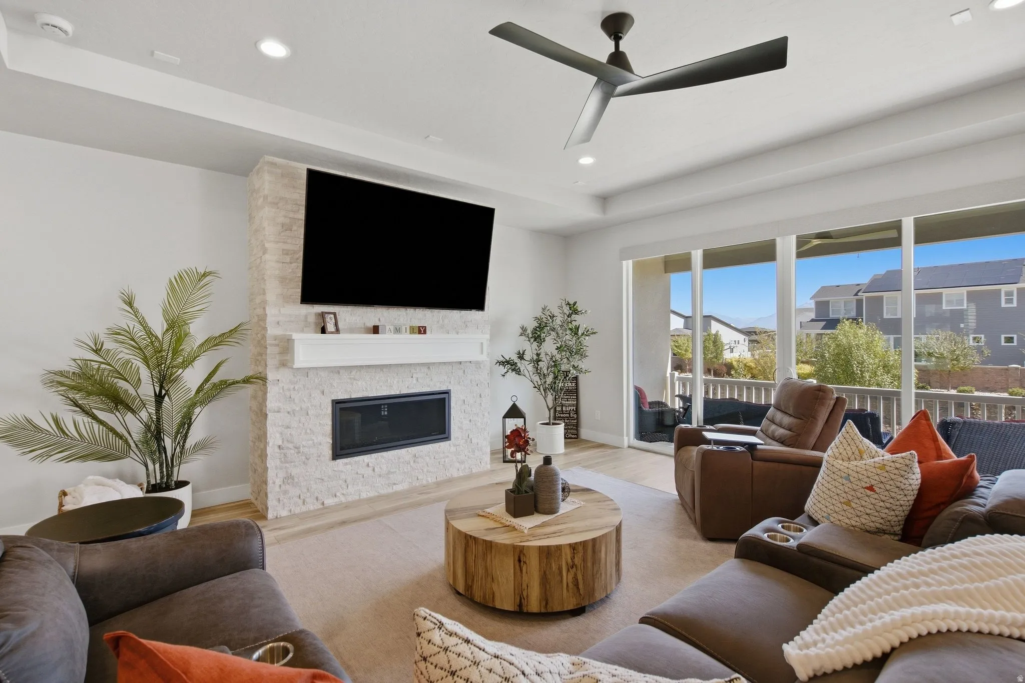 Living area featuring a stone-faced fireplace with a white mantel, recessed ceiling lighting, a contemporary ceiling fan, and large sliding glass doors opening to an exterior patio.