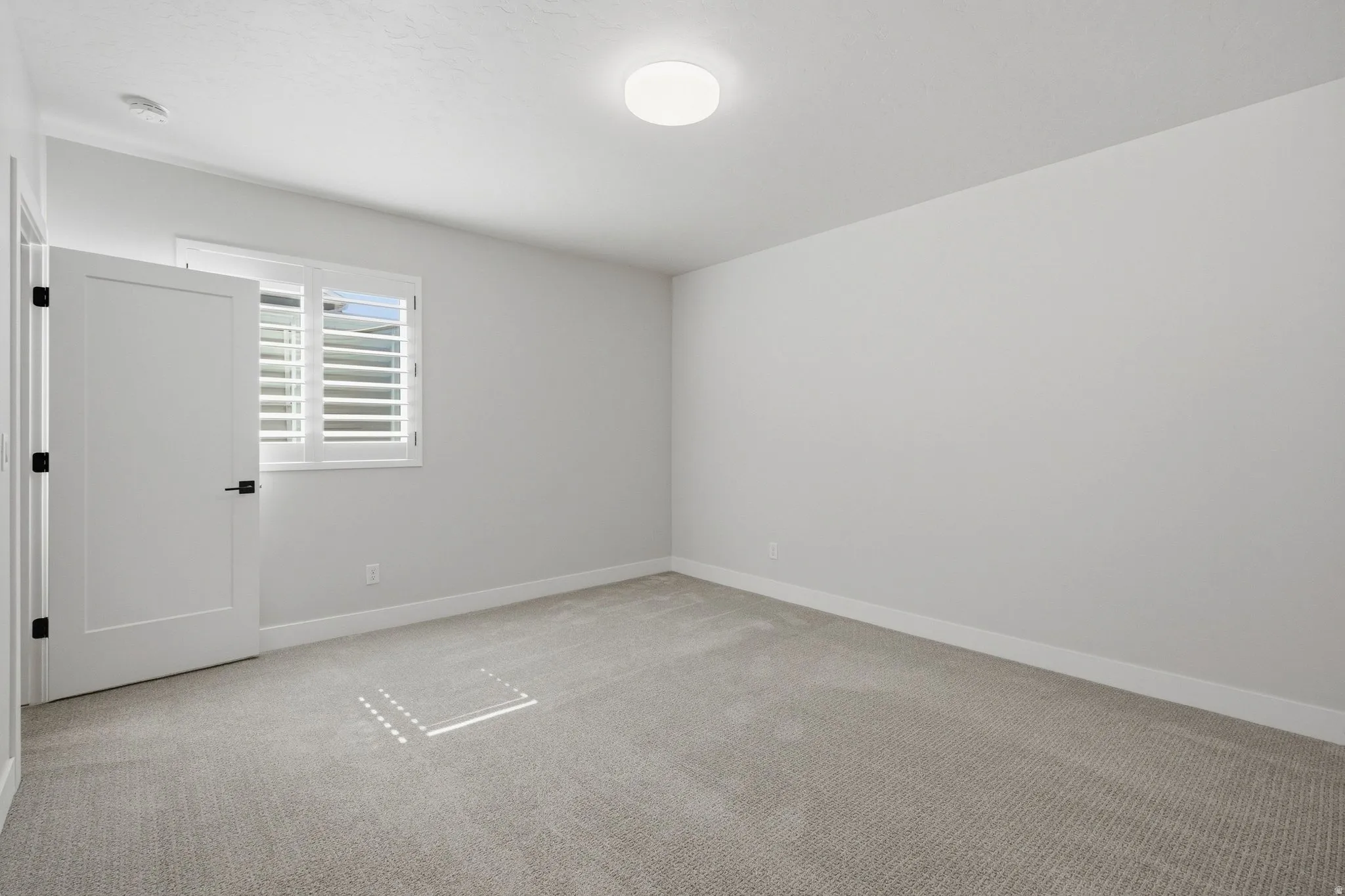 Neutral wall paint, plush carpeting, white interior door with matte black hardware, shutters, and a flush-mount ceiling light.