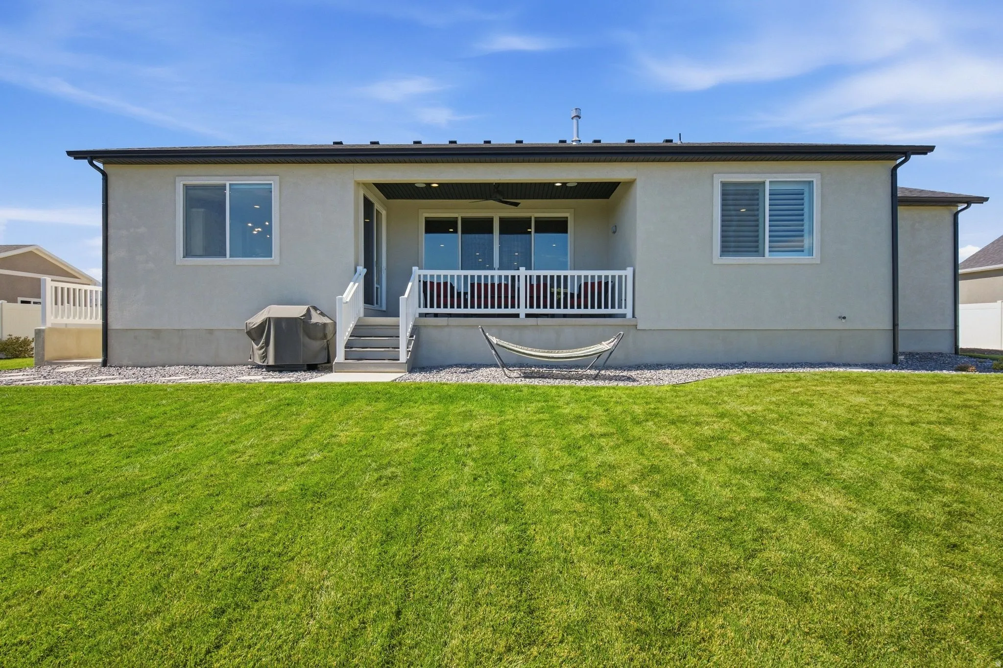 Expansive green lawn, elevated covered patio, white railing, sliding glass doors, and stucco exterior.
