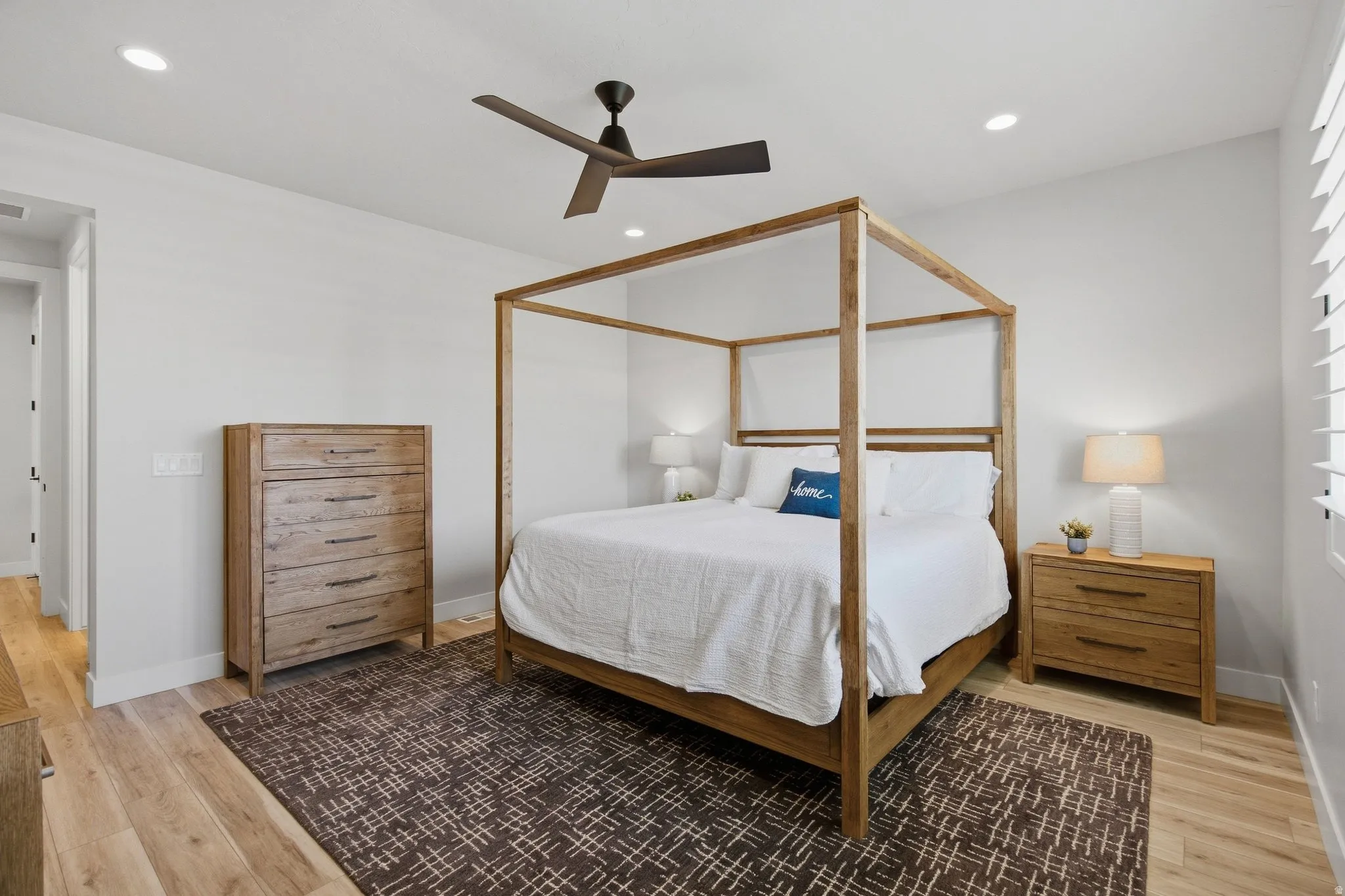 Primary bedroom with recessed lighting, ceiling fan, wood-finish flooring, white walls, and window with shutters.