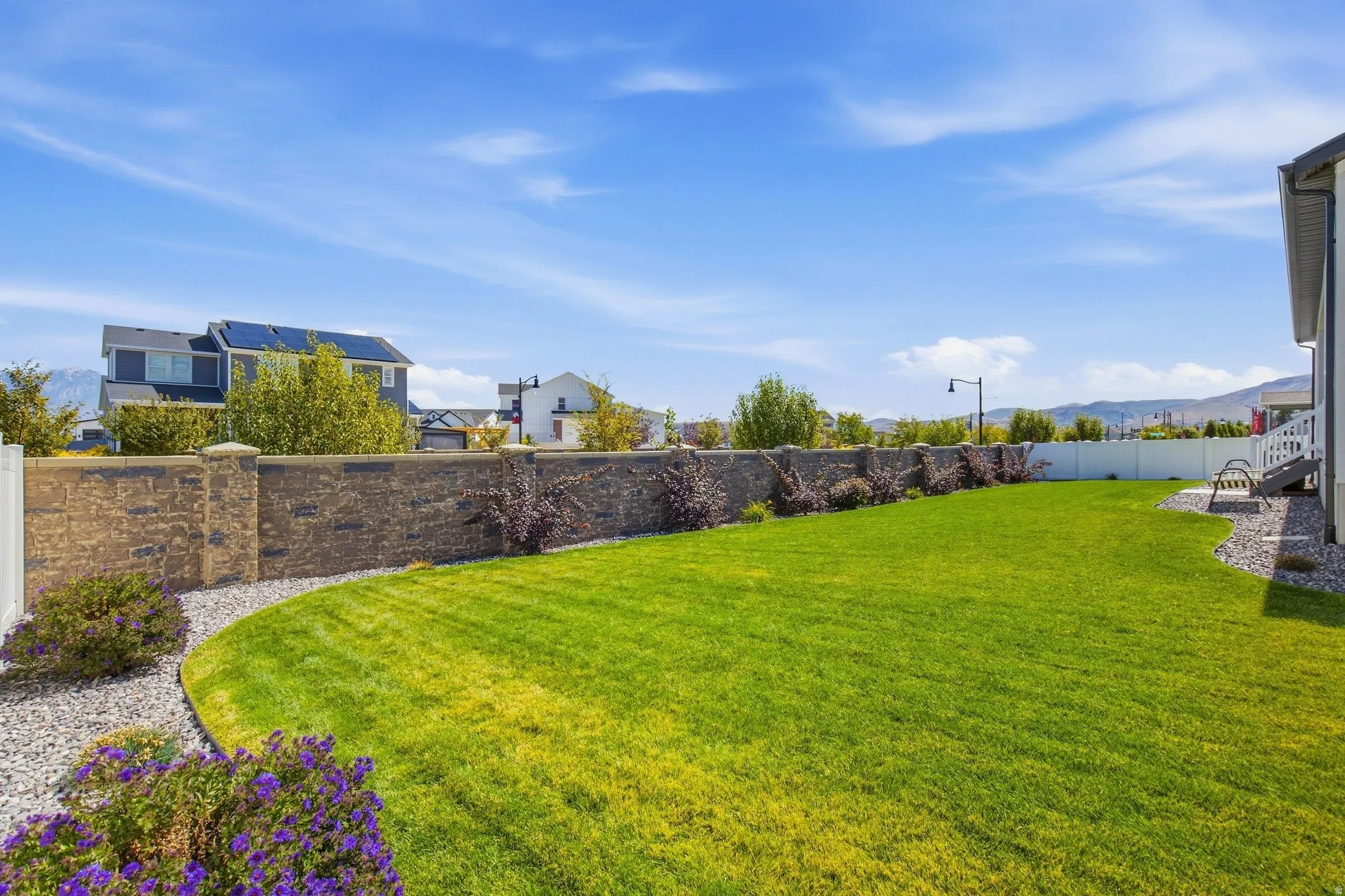 Spacious yard featuring a lush lawn, a decorative stone wall, and a white privacy fence.