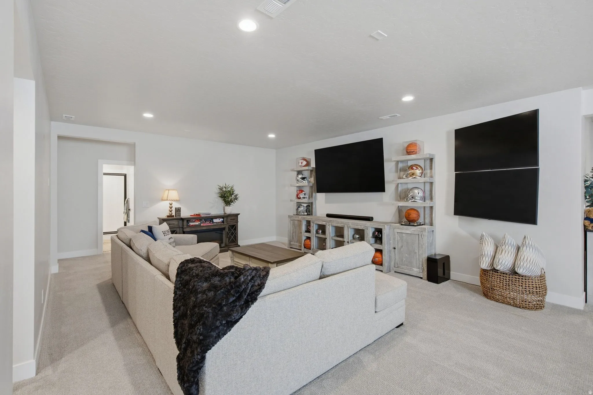 Recessed lighting illuminates this expansive room, featuring light-toned carpeting and substantial white baseboards.