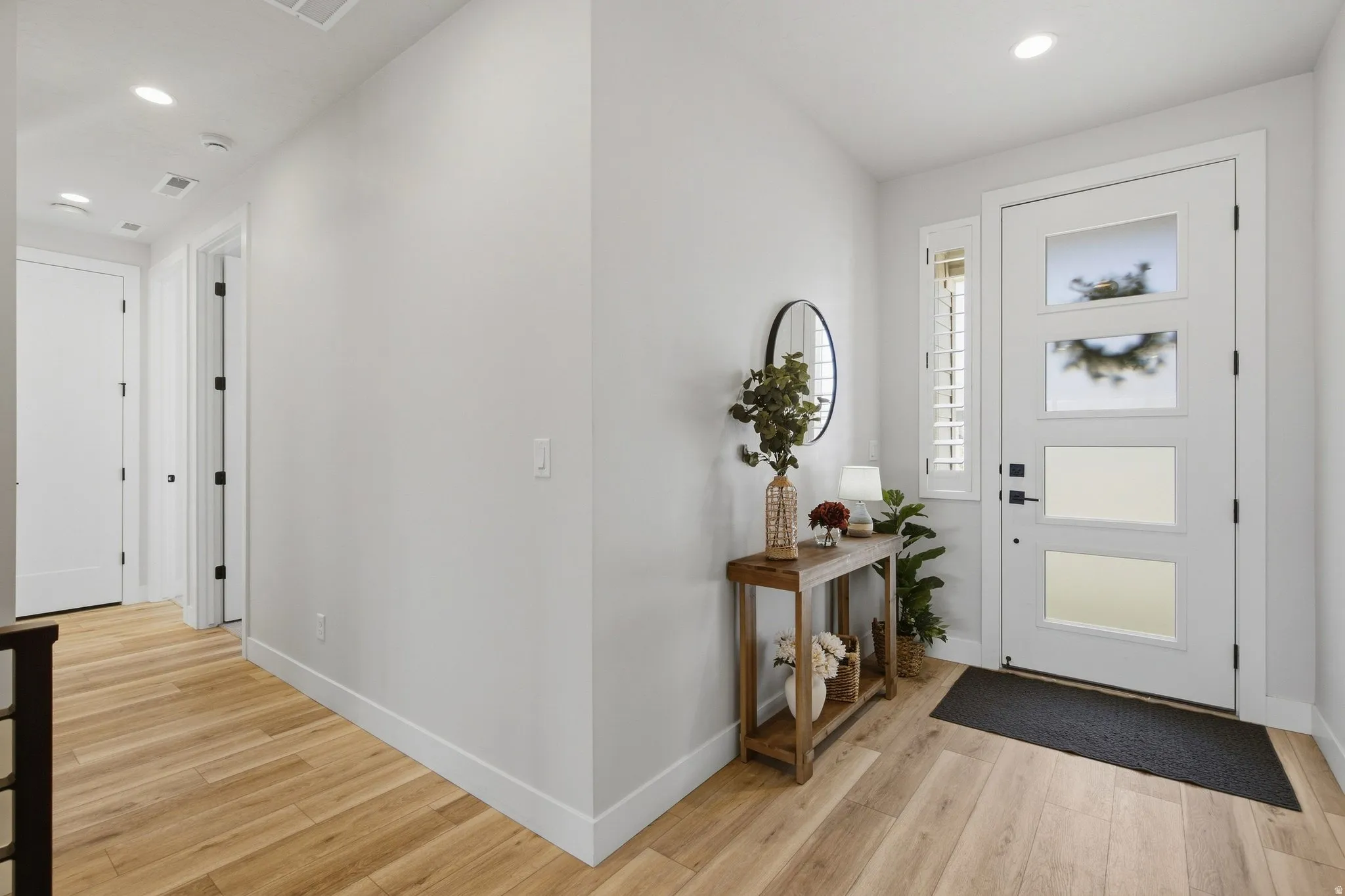 Entryway featuring LVP flooring, a contemporary front door with multiple glass panes, a sidelight with plantation shutters, recessed ceiling lighting, and a neutral wall color.