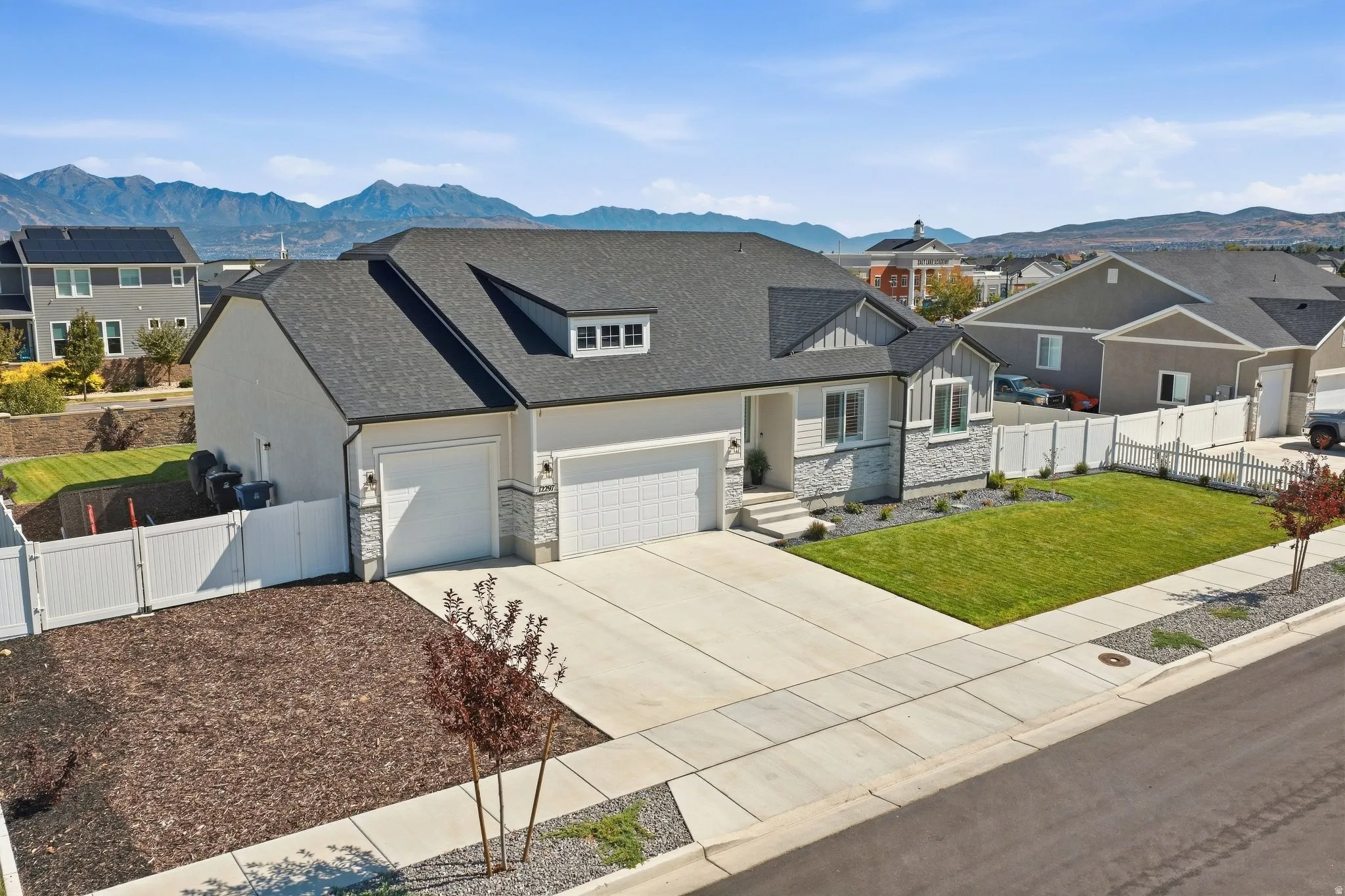 Contemporary residence featuring a 4-car garage, stone and siding exterior, manicured lawn, and mountain backdrop.