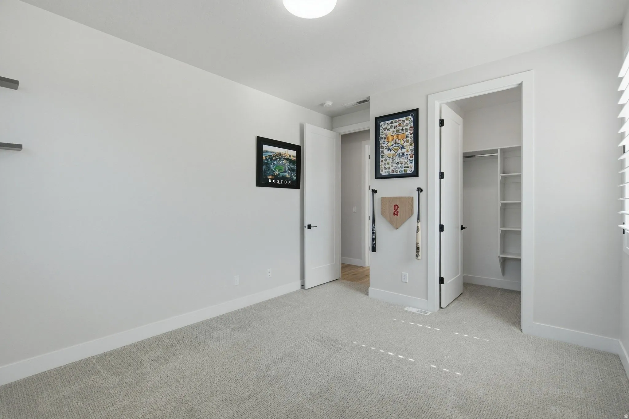 White walls, light-colored carpet flooring, white trim, and a built-in closet with shelving.