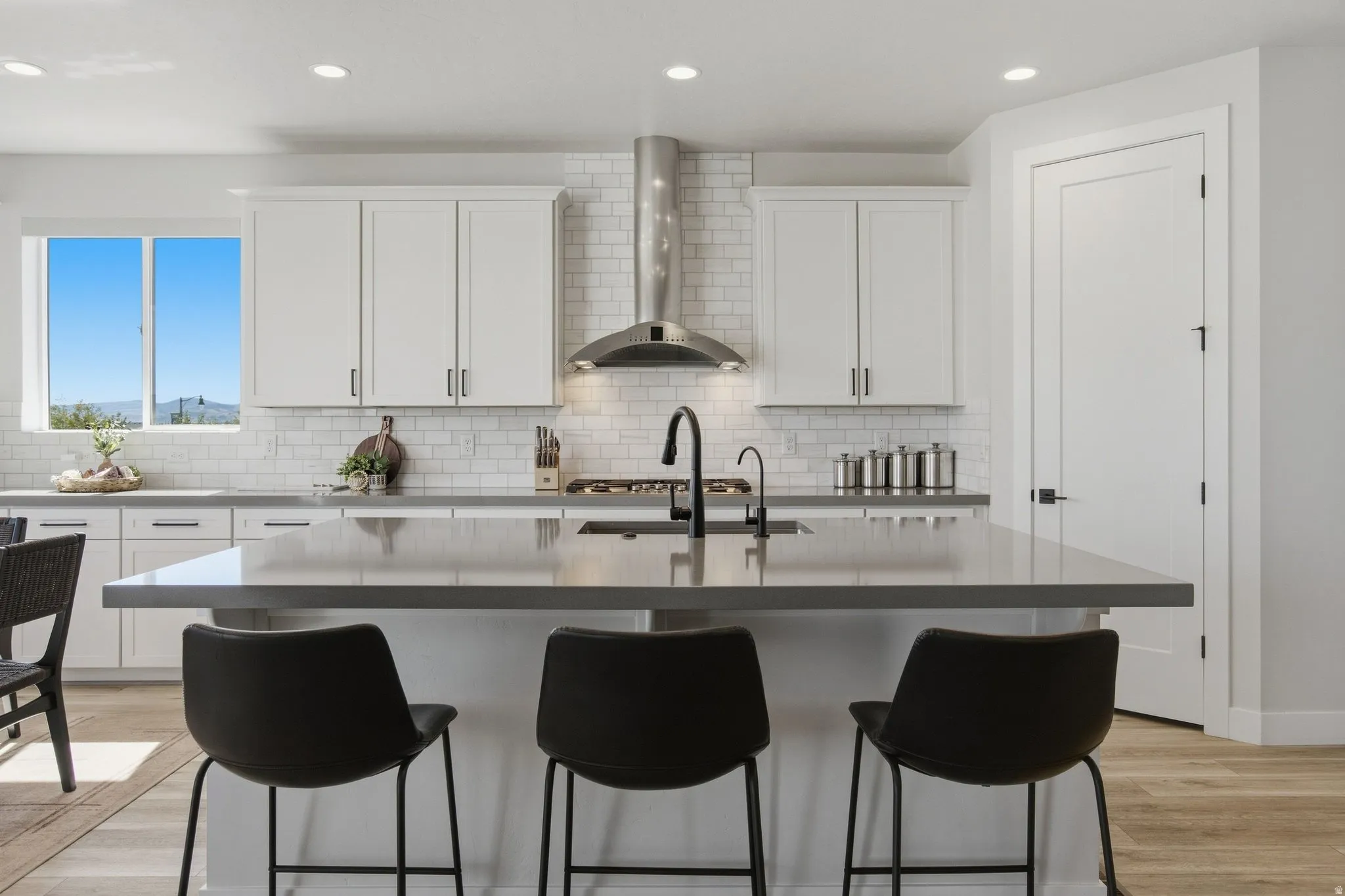 Kitchen featuring an expansive center island, modern white cabinetry, subway tile backsplash, stainless steel range hood, and LVP wood-finish flooring.