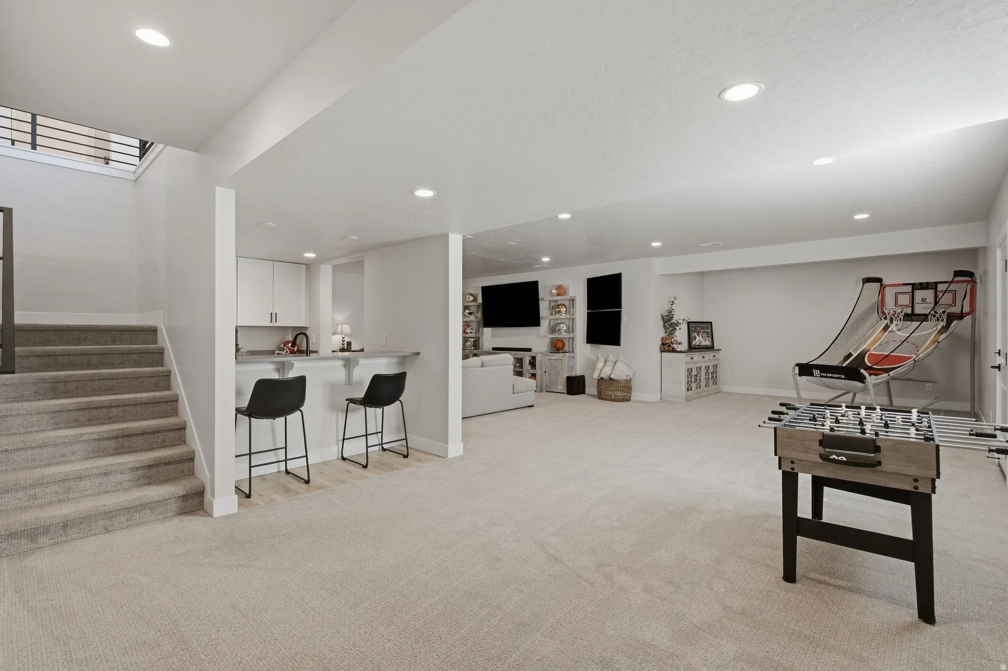 Spacious recreation area featuring recessed lighting, a built-in wet bar with white cabinetry, and a carpeted staircase.