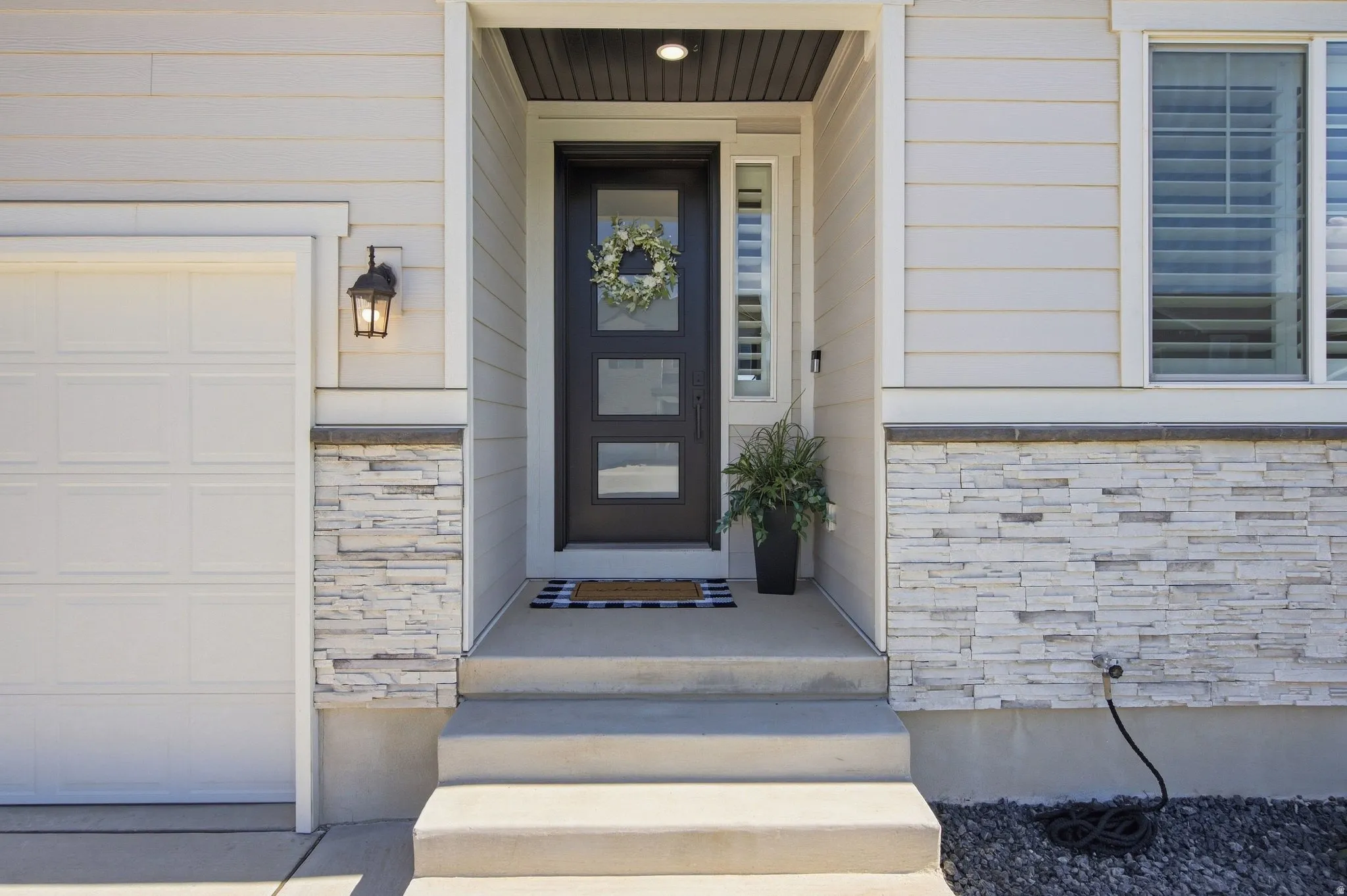 Light-toned horizontal siding with stacked stone accents.