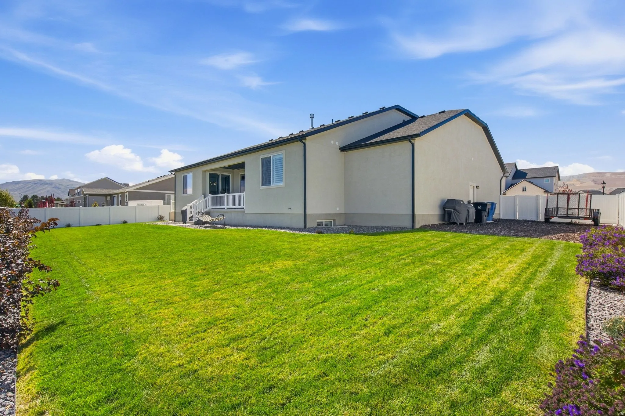 Expansive green lawn, white vinyl fencing, and a rear patio with white railings.