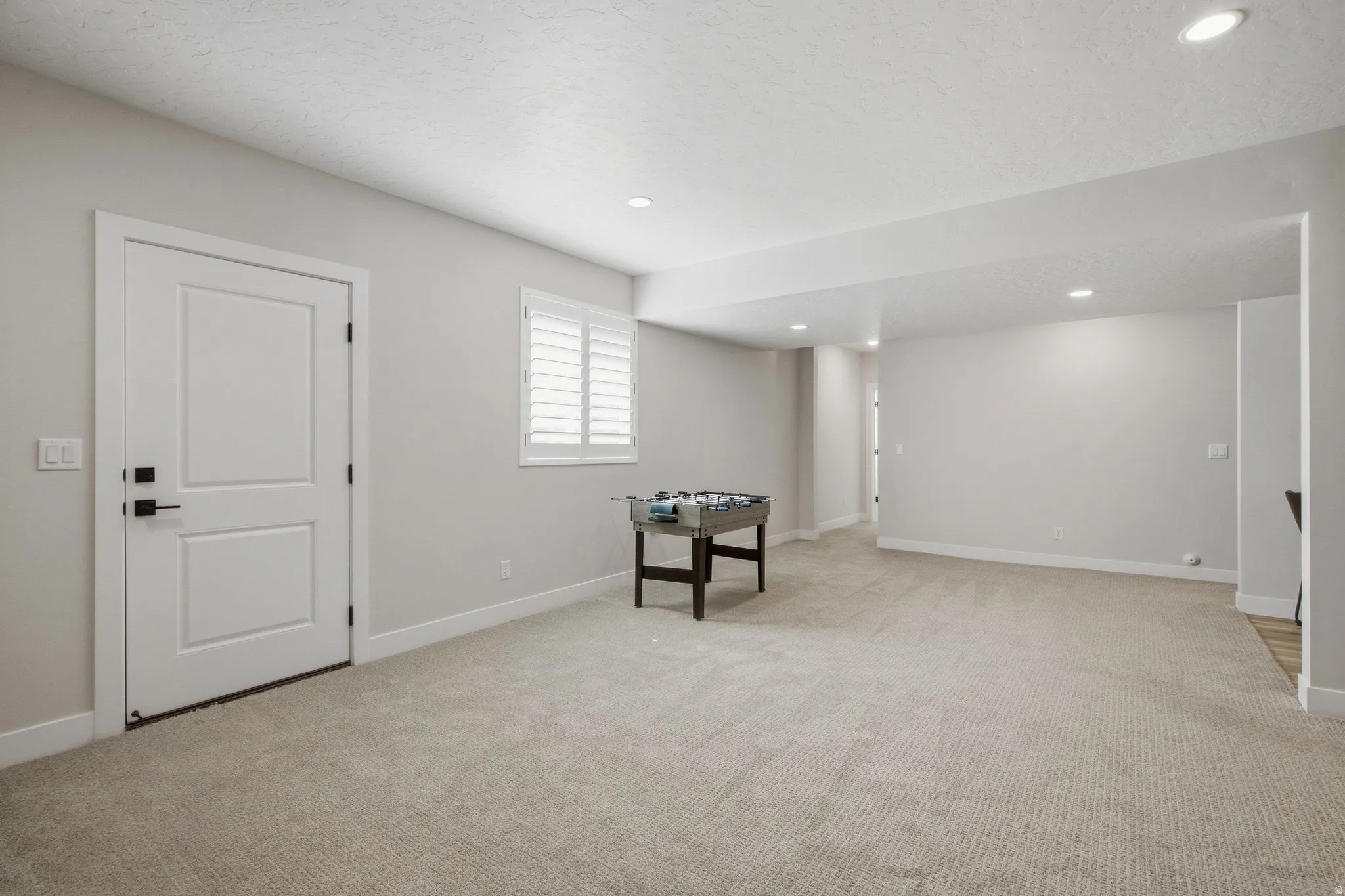 Separate basement entrance with recessed lighting, light-toned carpeting, window with plantation shutters, white interior door with black hardware, and light-colored walls.