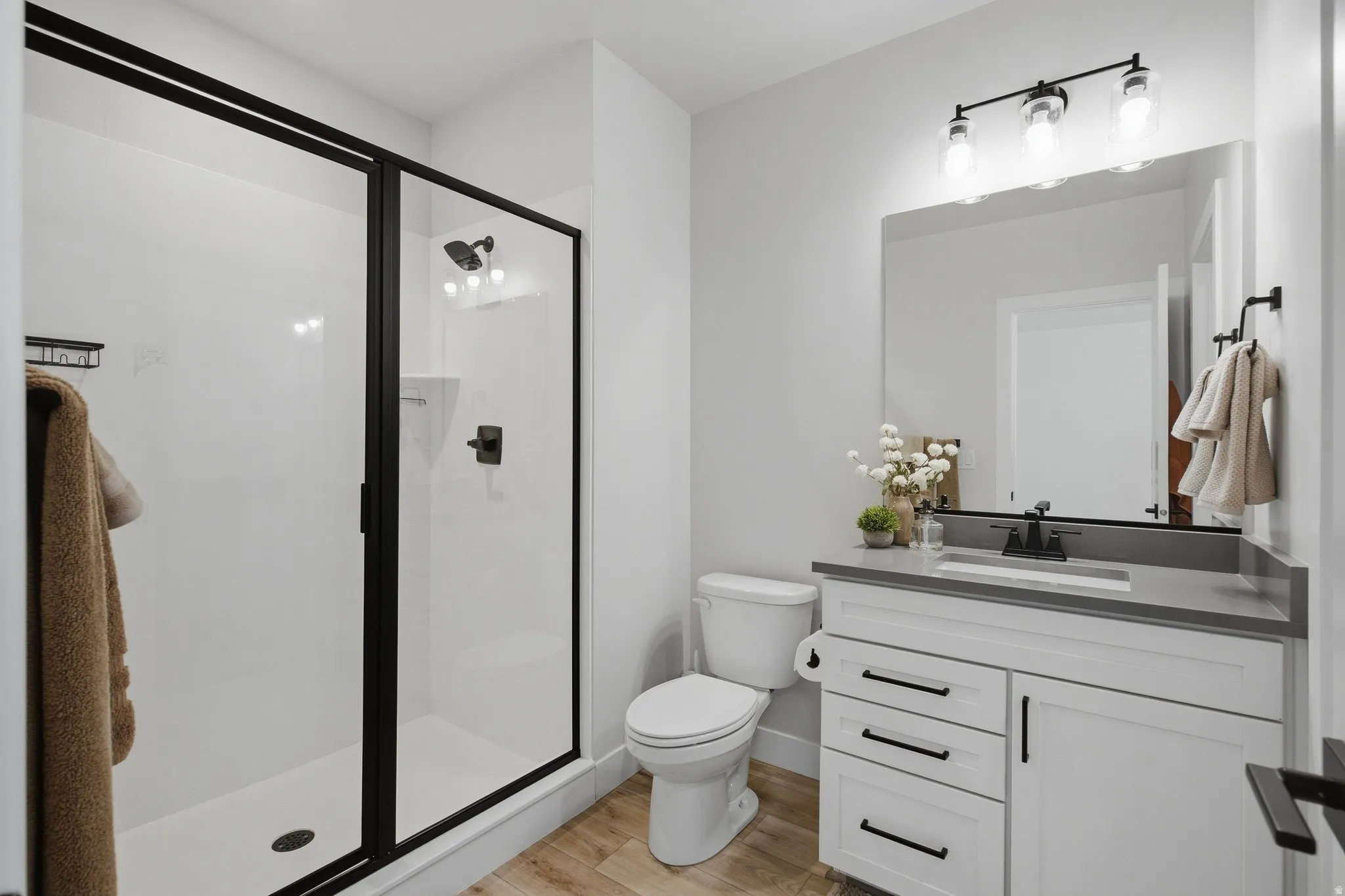 Modern 3/4 bathroom featuring a white vanity with dark hardware, a large glass enclosed shower, and a gray countertop.