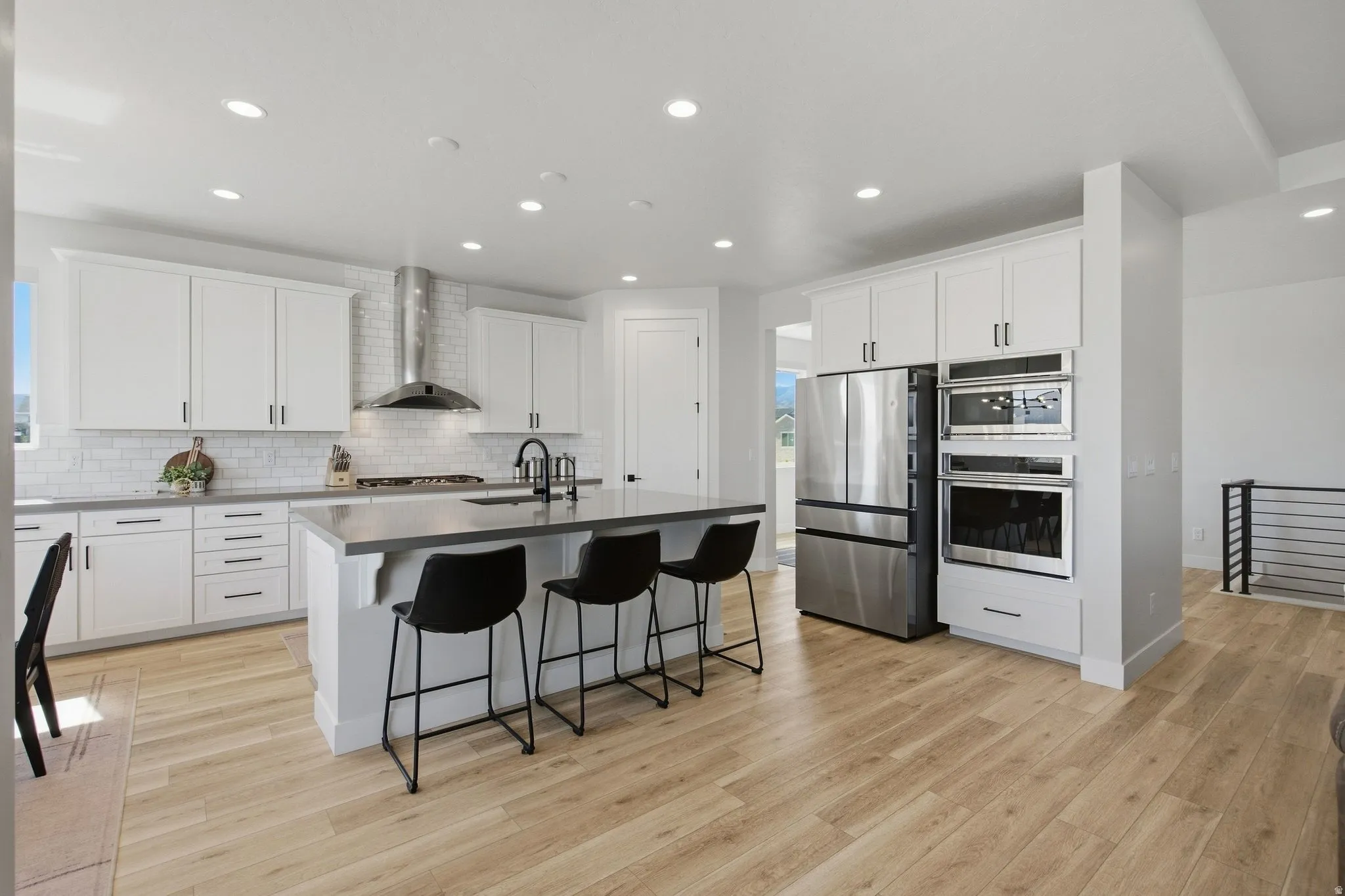 Modern kitchen featuring light LVP wood-finish flooring, white cabinetry, stainless steel appliances, a center island with a sink, and recessed lighting.