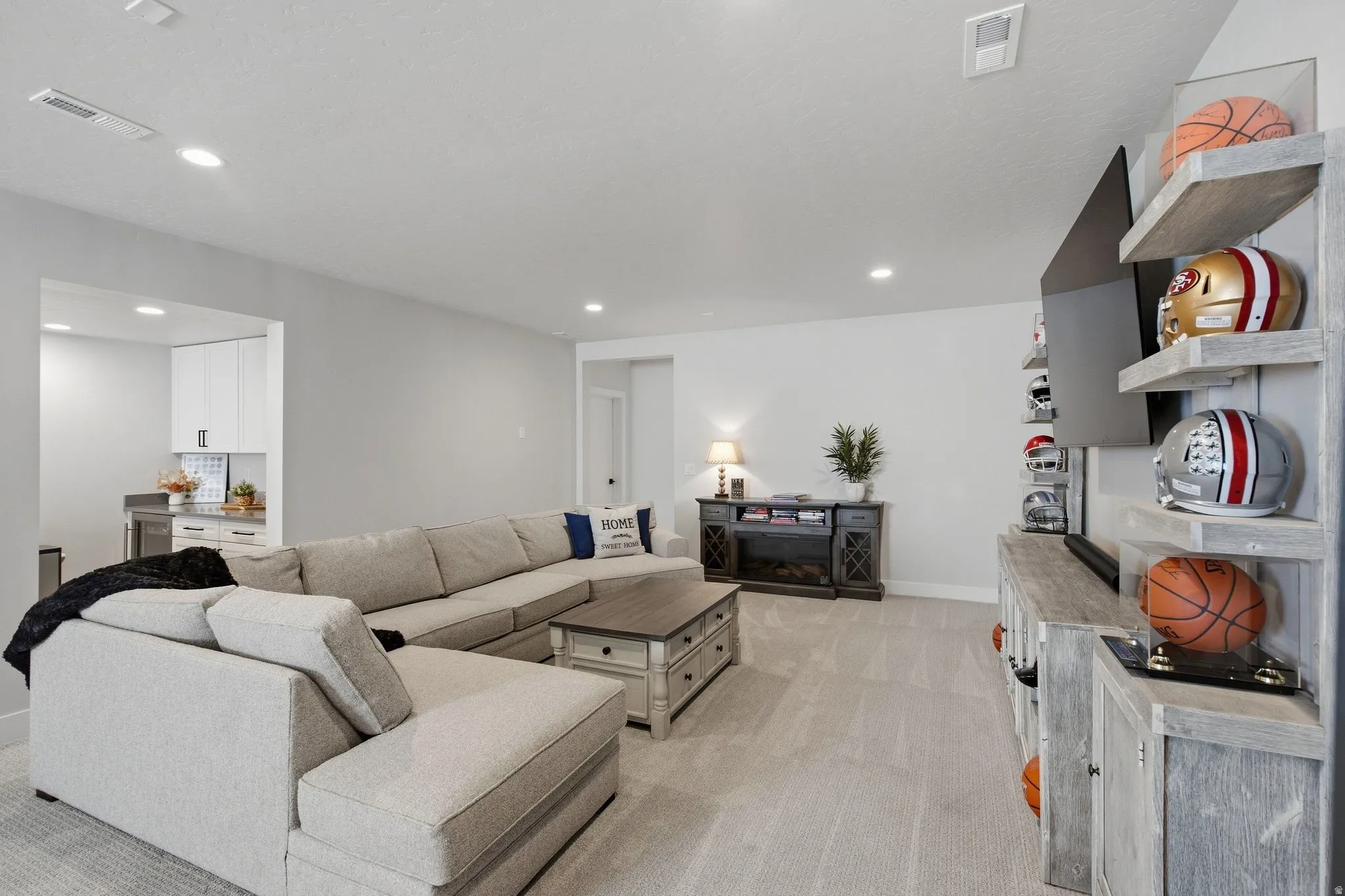 Recessed lighting, light-toned carpeting, and a dedicated wet bar area with white cabinetry.