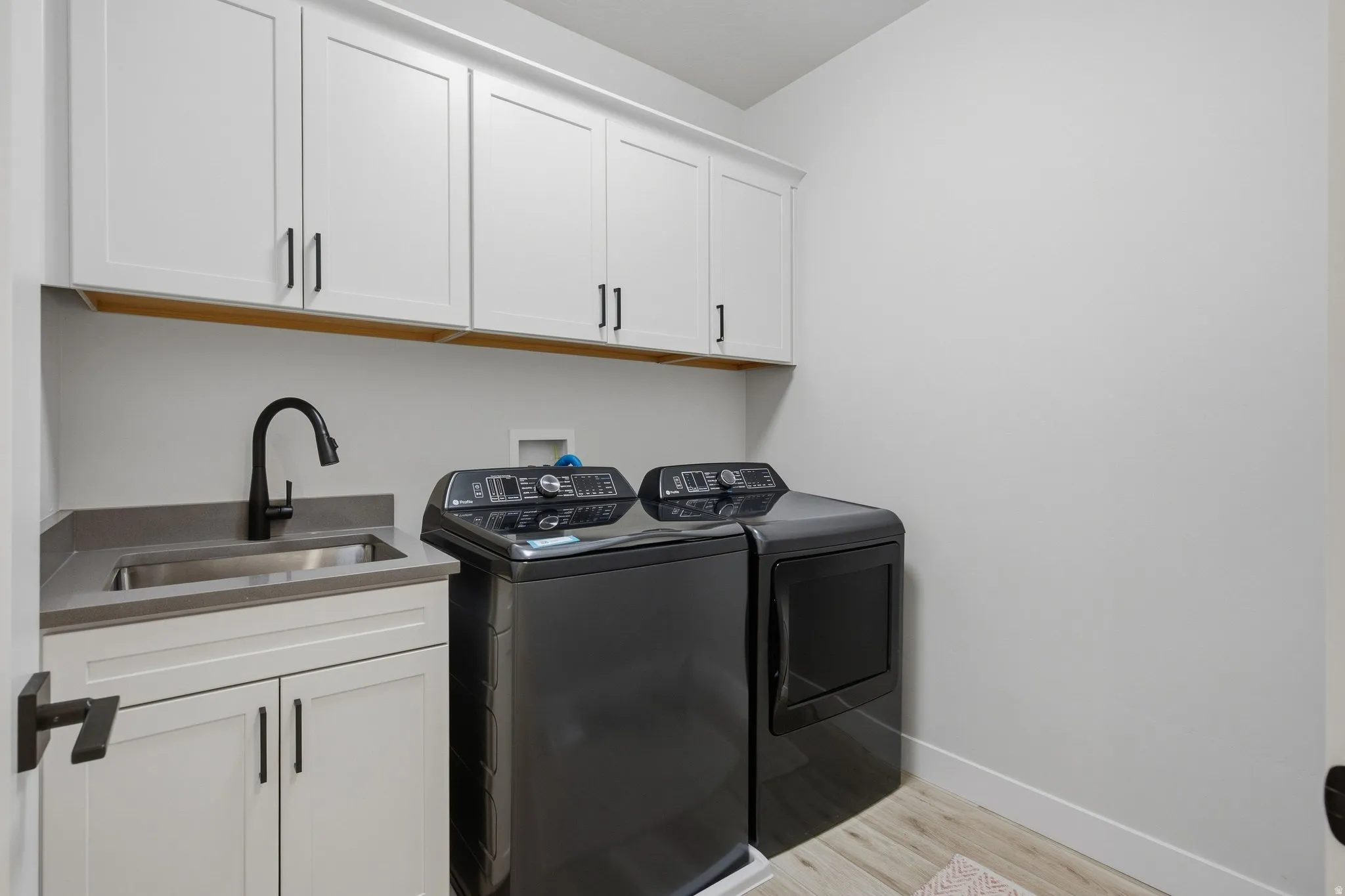 White cabinetry with black hardware, stainless steel sink, dark countertop, and LVP wood-finish flooring.