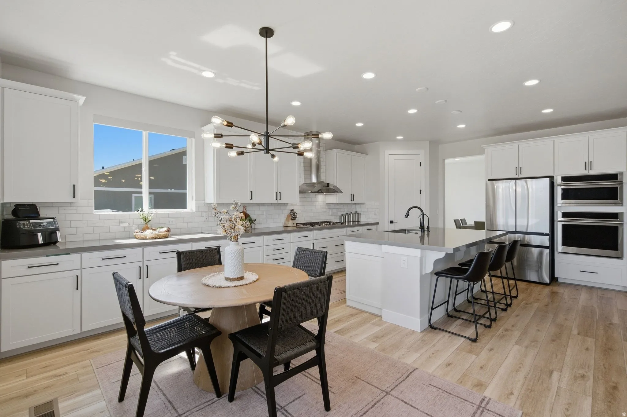Spacious kitchen featuring an expansive island with seating, stainless steel appliances, white cabinetry, and LVP wood-finish flooring.