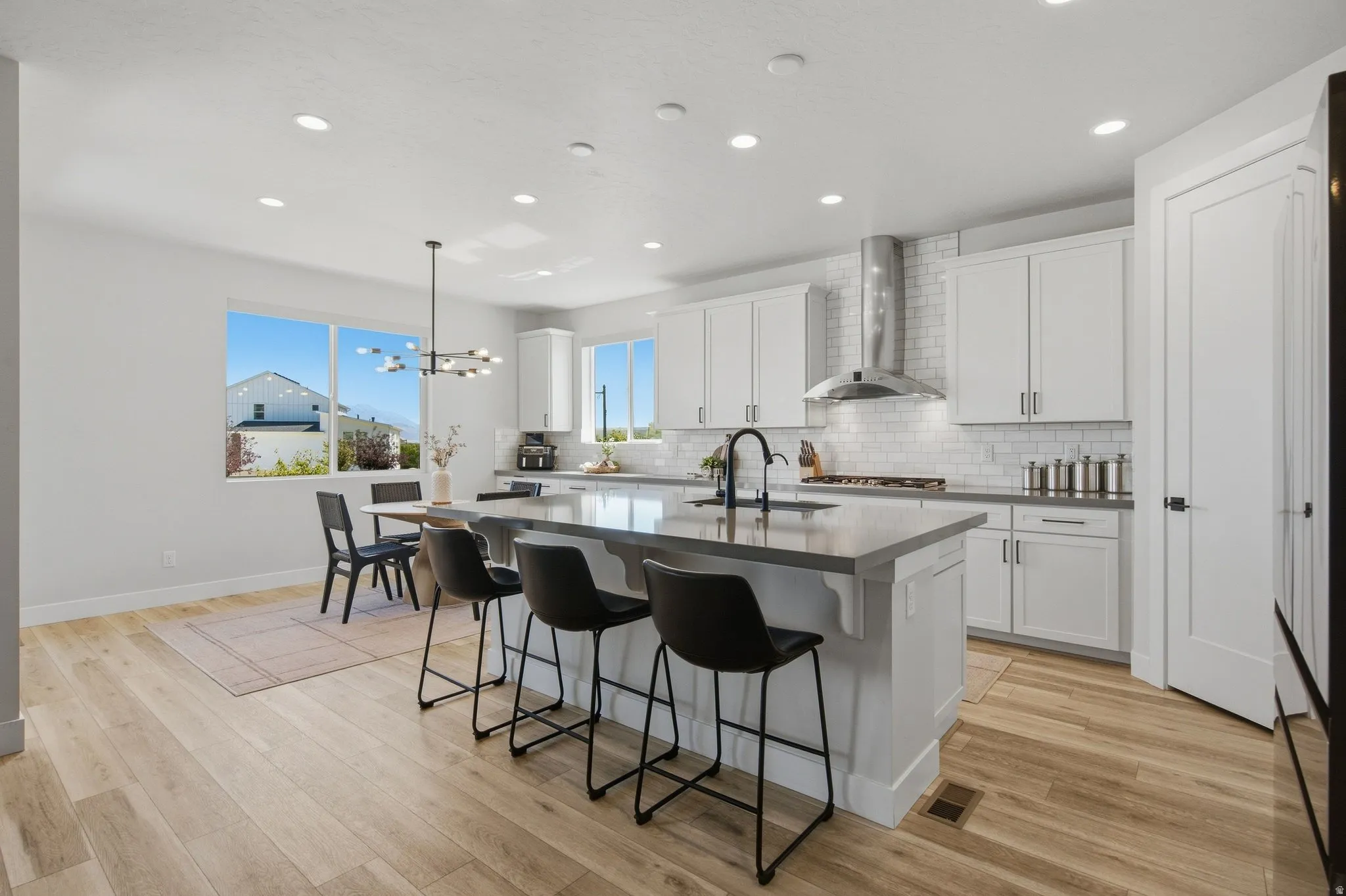 Spacious kitchen featuring an expansive center island, white cabinetry, subway tile backsplash, and light LVP wood-finish flooring.