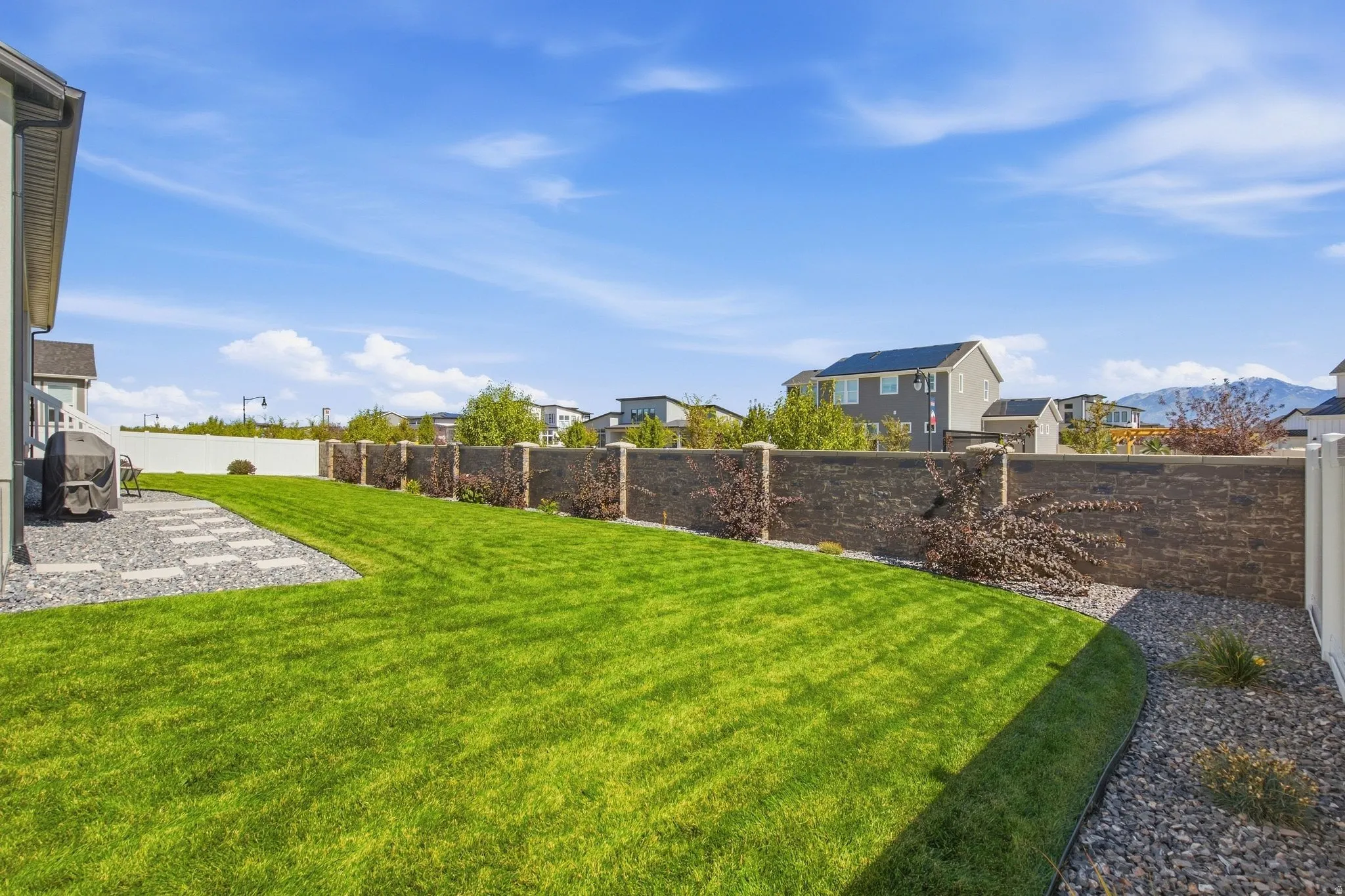 Expansive green lawn with a paver pathway, mature plants, and a privacy fence.