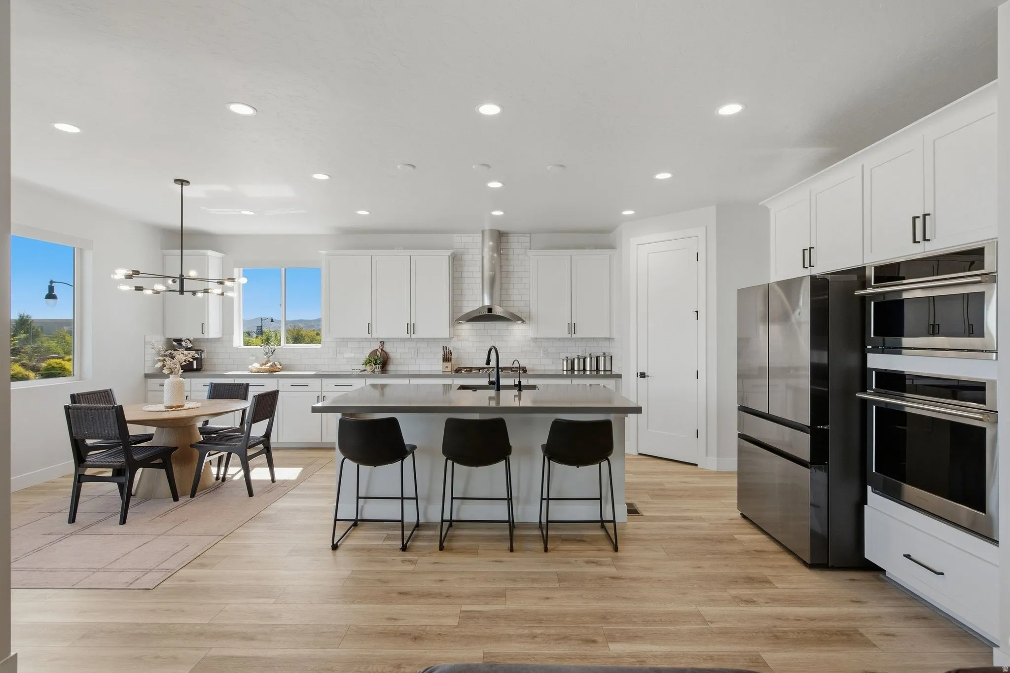 White cabinetry with black hardware, stainless steel appliances, LVP wood-finish flooring, recessed lighting, and a kitchen island with seating.