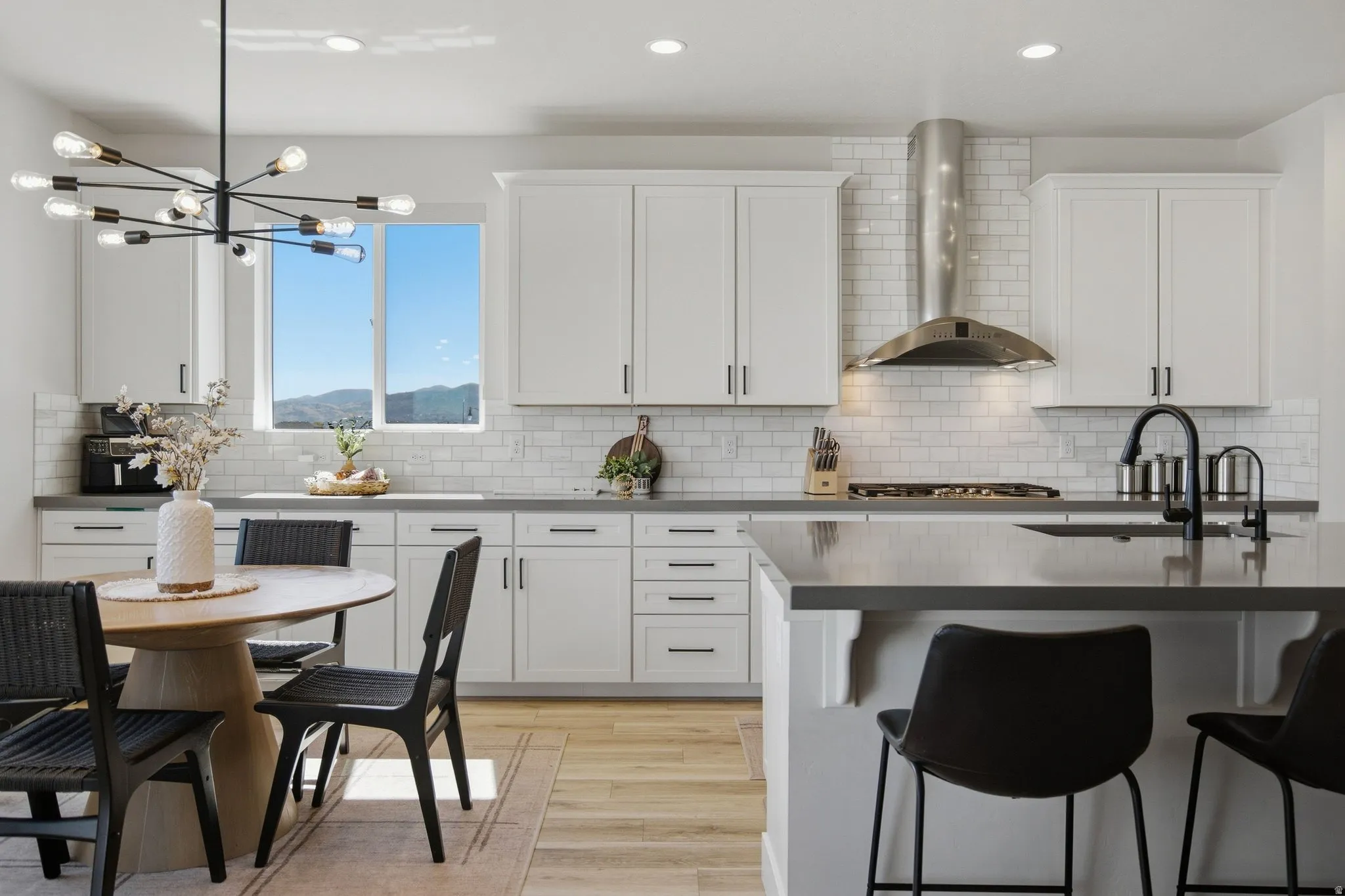 White cabinetry, light LVP wood-finish flooring, subway tile backsplash, stainless steel range hood, and a kitchen island with seating.