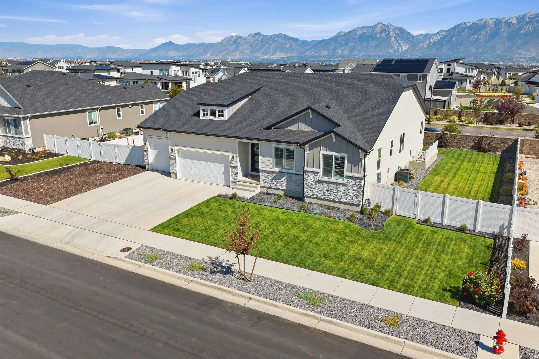 Contemporary home with a dark shingle roof, stone and siding exterior, a 4 -car garage, fully fenced with a manicured lawn.