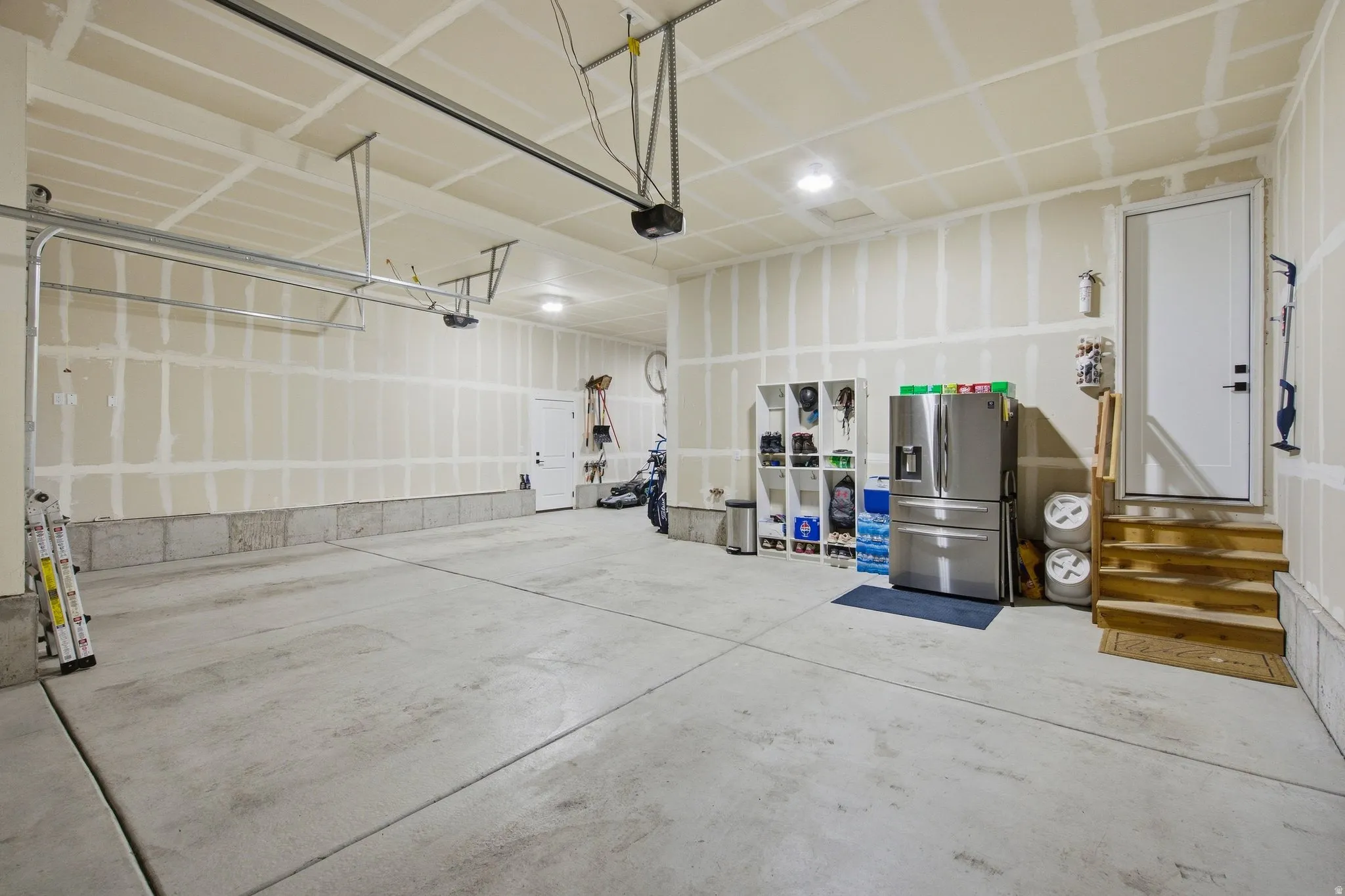 Spacious garage with concrete flooring, and a built-in staircase leading to the interior doorway.