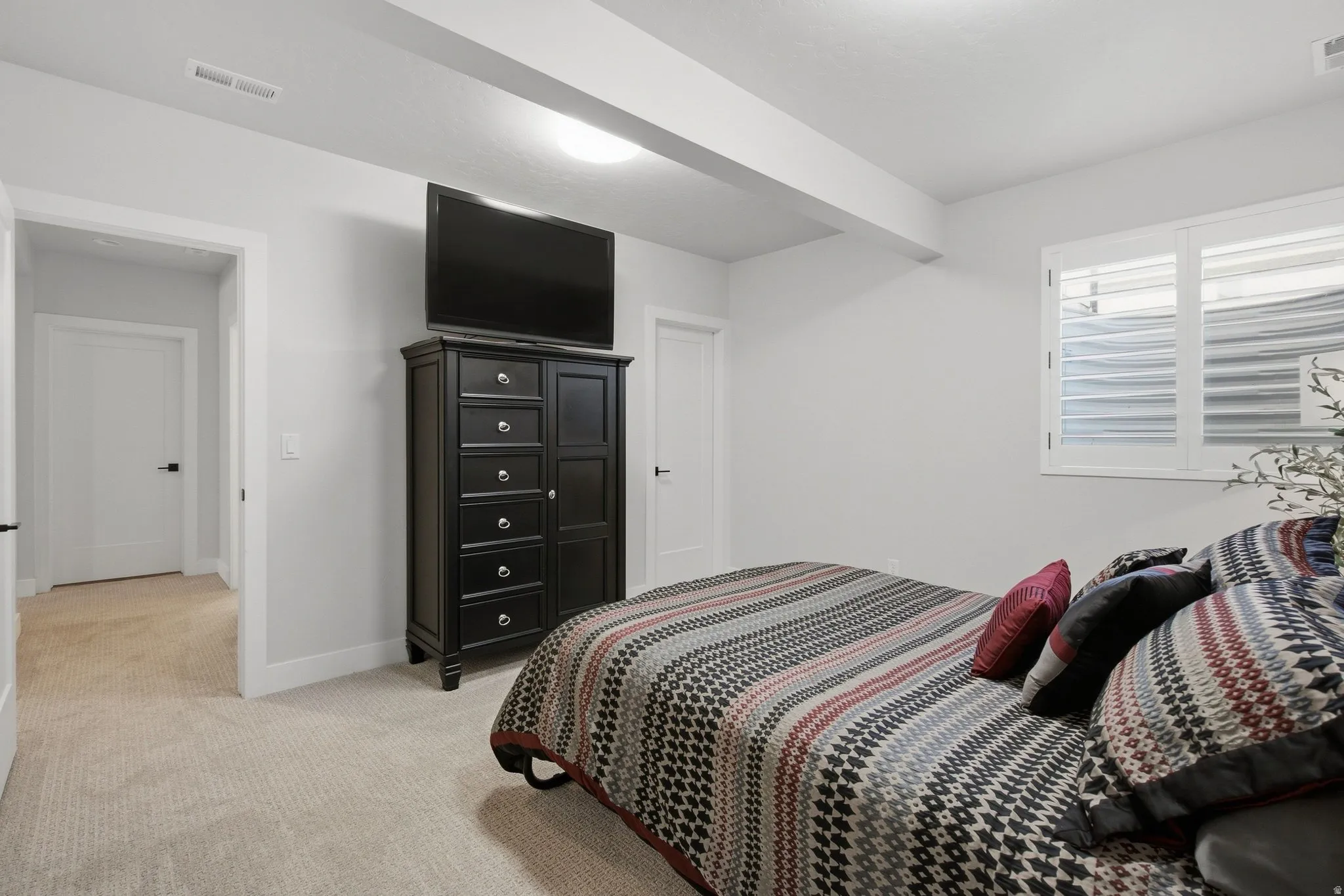 Recessed lighting illuminates the space, featuring light-colored carpeting, white walls, and a window with white shutters.
