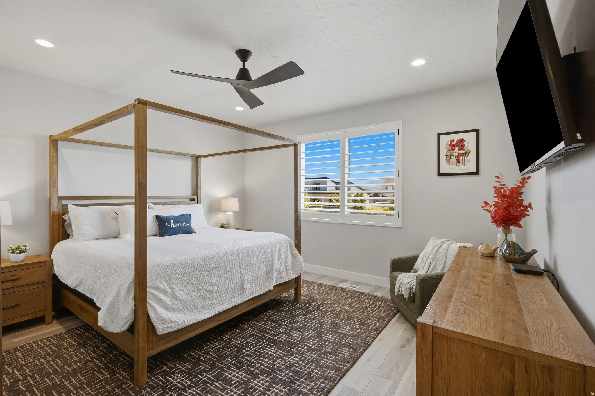 Primary bedroom with recessed lighting, ceiling fan, plantation shutters, LVP wood-finish flooring.