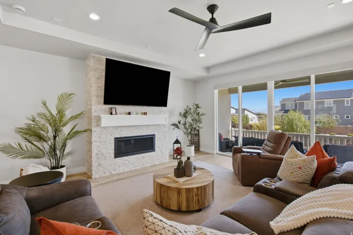 Living area featuring a stone-faced fireplace with a white mantel, recessed ceiling lighting, a contemporary ceiling fan, and large sliding glass doors opening to an exterior patio.