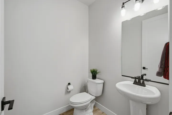 Half bath with pedestal sink with a dark faucet, wall-mounted mirror, and overhead lighting.