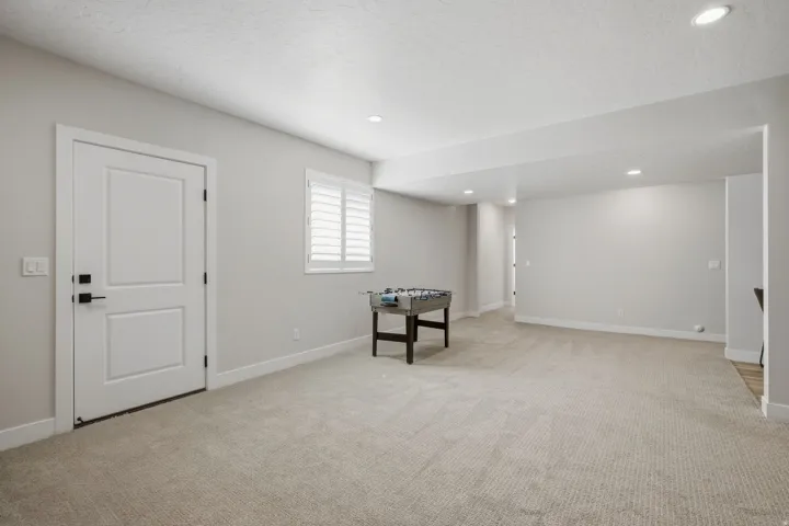 Separate basement entrance with recessed lighting, light-toned carpeting, window with plantation shutters, white interior door with black hardware, and light-colored walls.