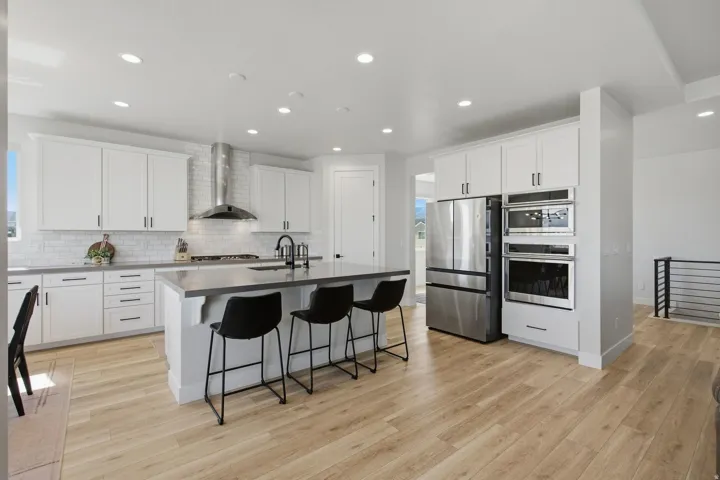 Modern kitchen featuring light LVP wood-finish flooring, white cabinetry, stainless steel appliances, a center island with a sink, and recessed lighting.