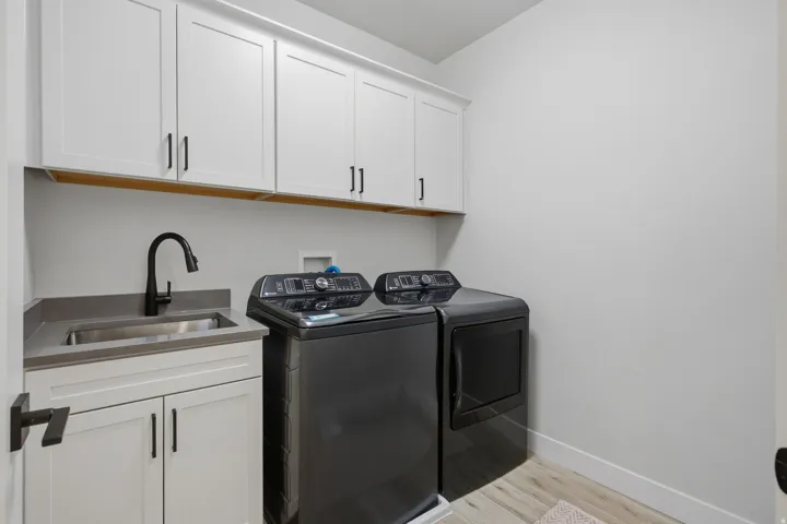 White cabinetry with black hardware, stainless steel sink, dark countertop, and LVP wood-finish flooring.