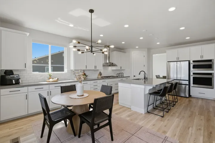 Spacious kitchen featuring an expansive island with seating, stainless steel appliances, white cabinetry, and LVP wood-finish flooring.