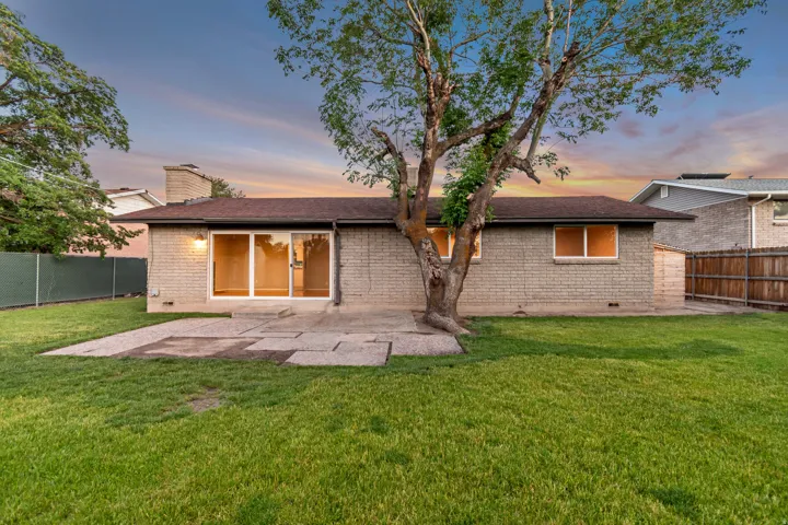 Expansive lawn area with a stone paver patio, brick exterior, sliding glass doors, and a mature tree