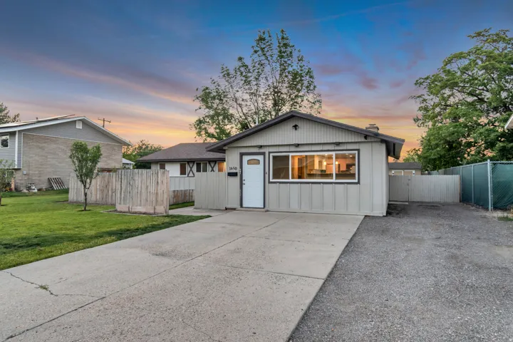 Single-story residence featuring light gray siding, a concrete driveway, and a gravel parking area
