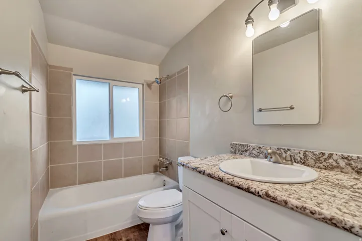 Bathroom featuring a vanity with an integrated sink, granite-style countertop, white cabinetry, and wood-finish flooring