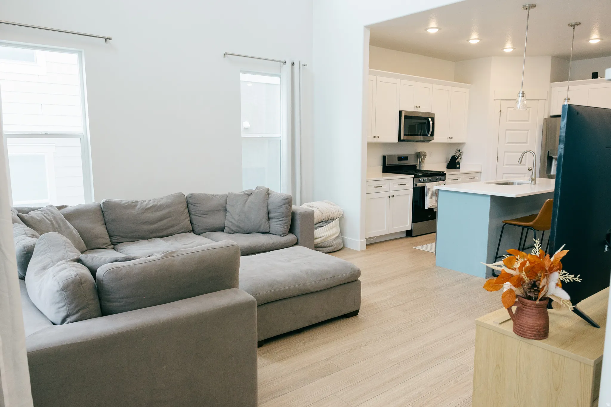 Recessed lighting, wood-finish flooring, white cabinetry, stainless steel appliances, and a kitchen island with pendant lighting