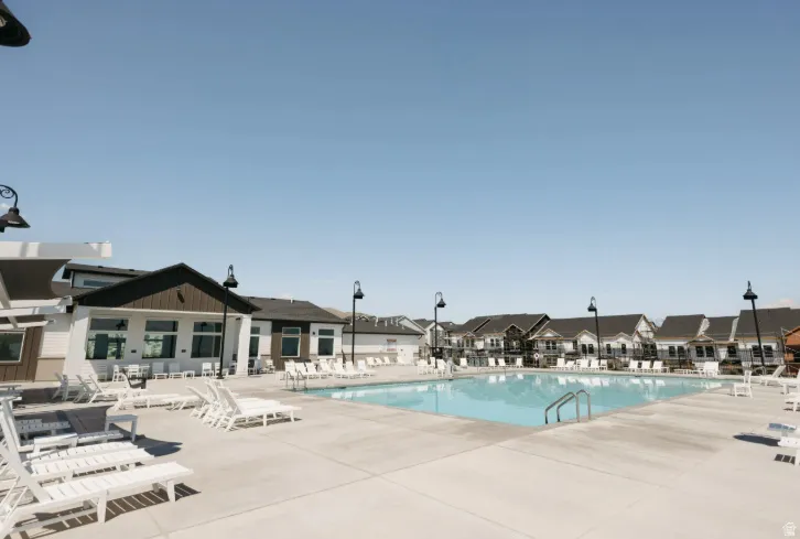 Expansive outdoor swimming pool with concrete decking, surrounded by lounge seating and a community building with large windows