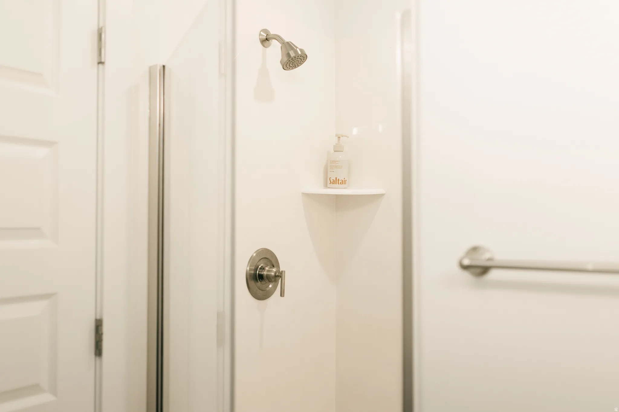 Shower with a brushed nickel showerhead, a single-handle temperature control, and a corner shelf