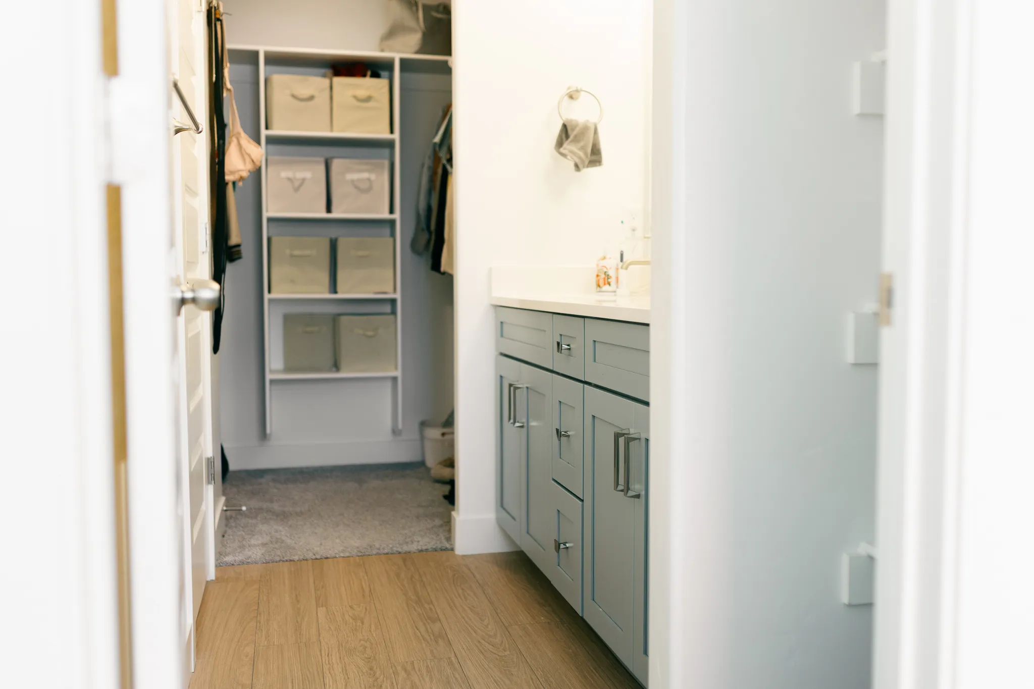 Wood-finish flooring, built-in closet shelving system, light gray cabinetry, wall-mounted faucet, and a clean white countertop