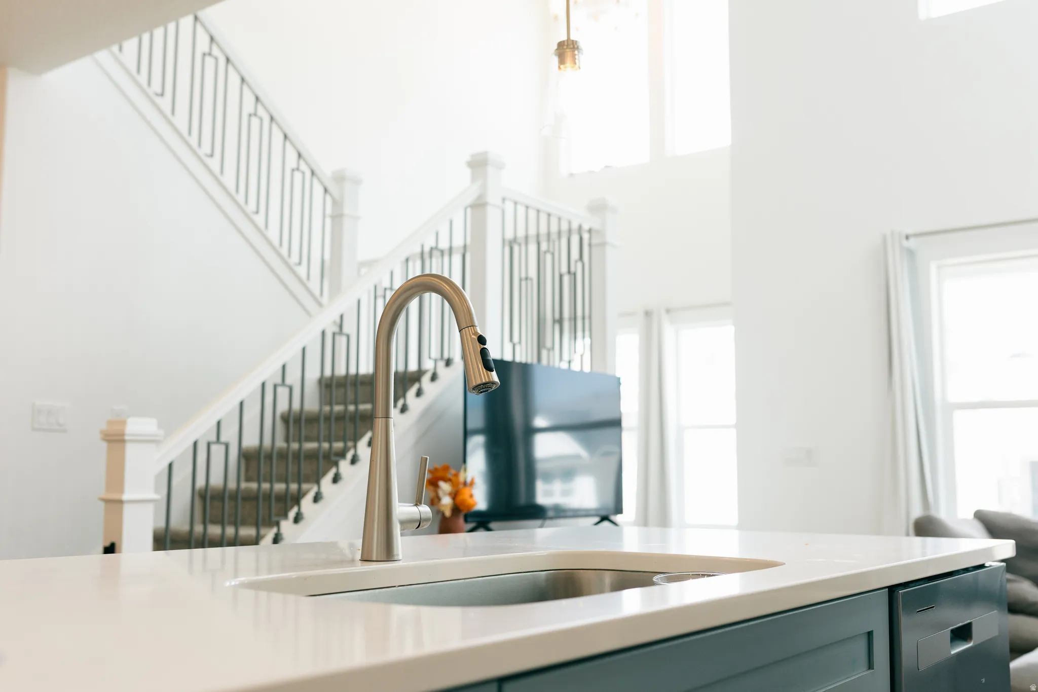 Kitchen island with a built-in sink, brushed nickel faucet, light-toned countertop, and integrated dishwasher