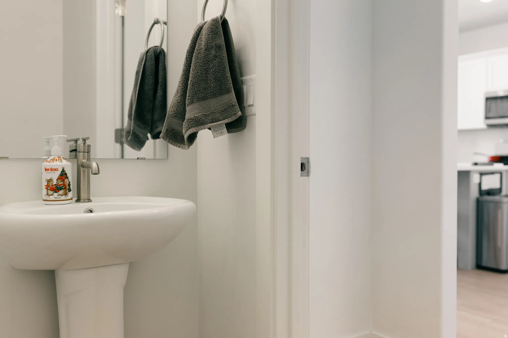 Pedestal sink with a brushed nickel faucet, wall-mounted mirror, and wood-finish flooring