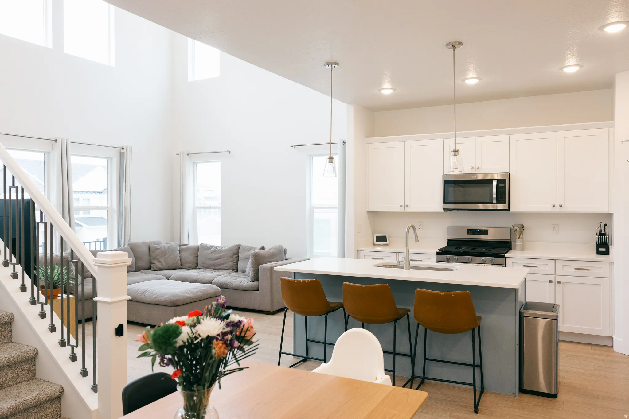 Open-concept living area featuring a kitchen island with seating, stainless steel appliances, white cabinetry, and wood-finish flooring